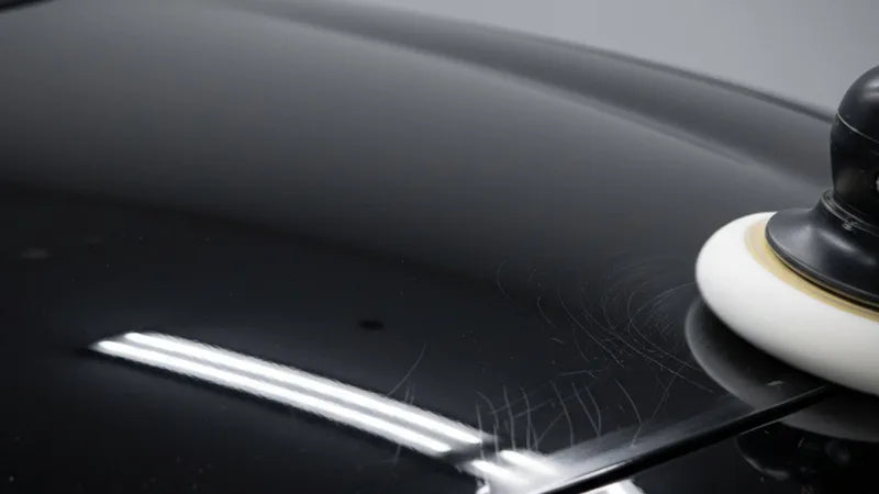 Hand die een one step polish aanbrengt op donkere autolak met een polishing pad