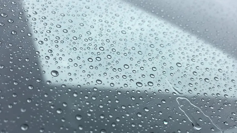 Waterdruppels die van een behandelde autoruit afrollen na aanbrengen regenafstoting auto