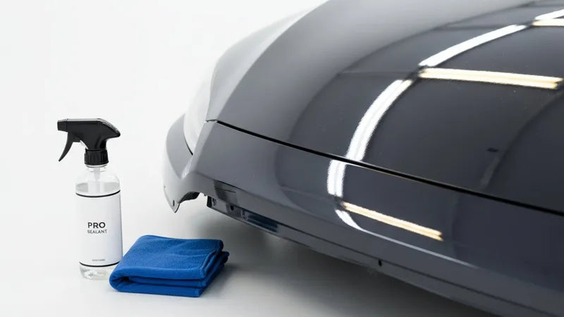 Hand die sealant aanbrengt op donkere autolak met een applicatorpad bij daglicht